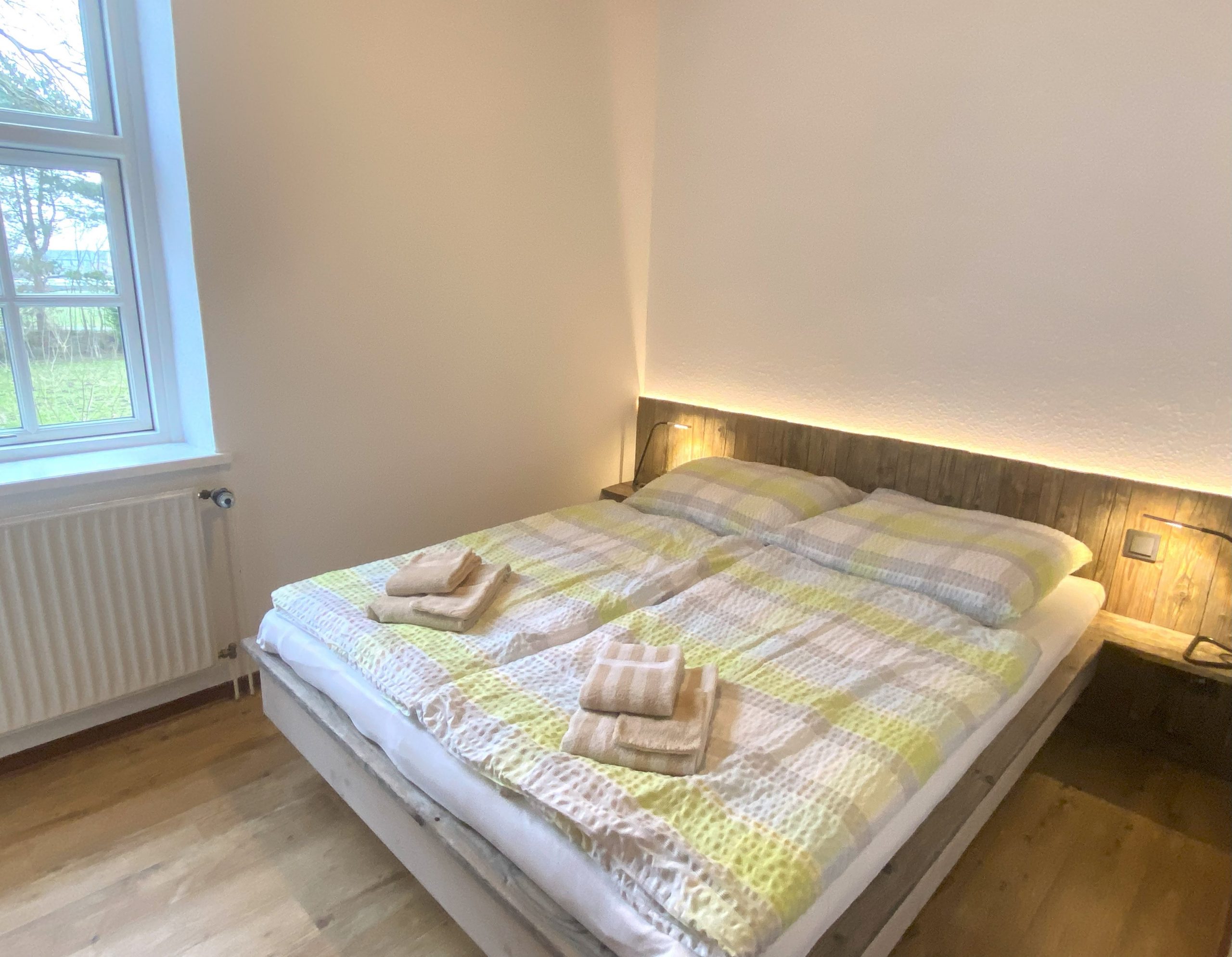 Helles Schlafzimmer mit großem Fenster und handgefertigtem Doppelbett aus Holz.