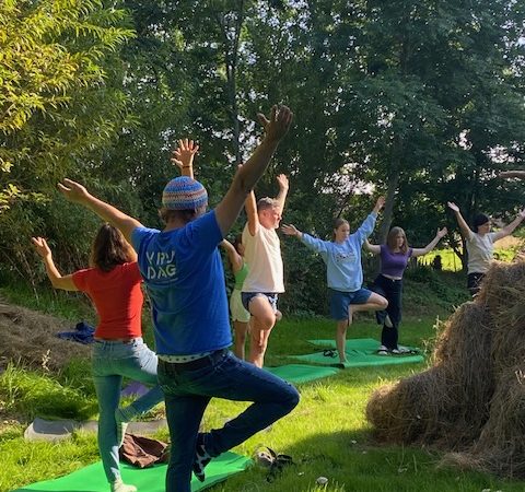 Menschen stehen auf einem Beim auf einer grünen Wiese und strecken die Arme weit aus